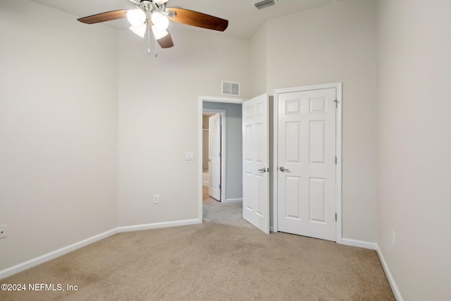 unfurnished room with light carpet, ceiling fan, and a high ceiling