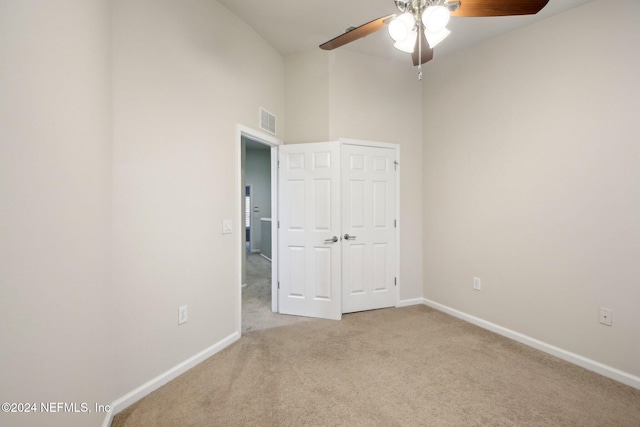 unfurnished room with light carpet, a towering ceiling, and ceiling fan