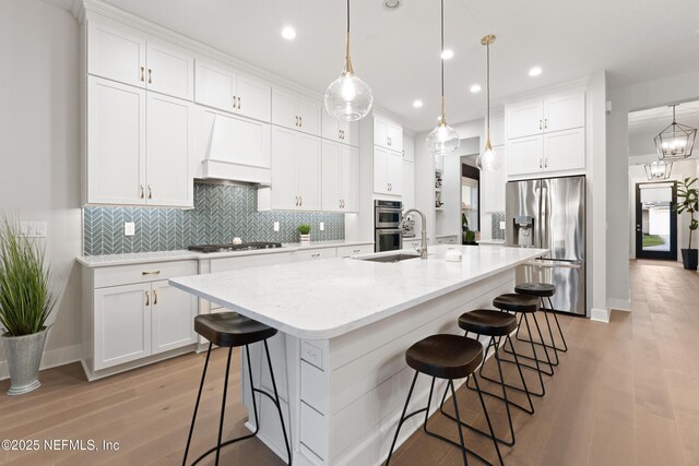 kitchen with light wood finished floors, custom range hood, white cabinets, and stainless steel appliances