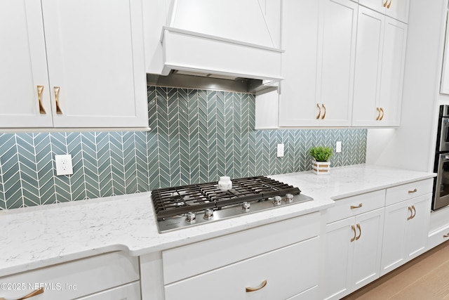 kitchen featuring premium range hood, backsplash, white cabinets, and appliances with stainless steel finishes
