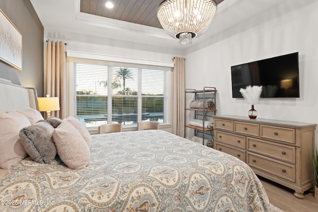bedroom with a raised ceiling, light wood-style floors, and a notable chandelier