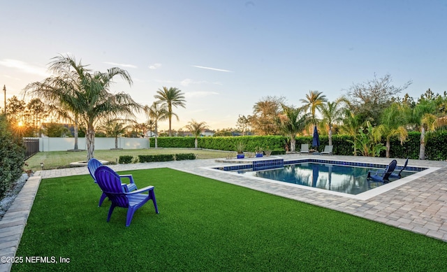 pool at dusk featuring a patio, a yard, a fenced backyard, and a fenced in pool