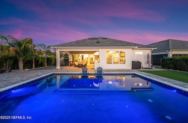 back of property at dusk featuring an outdoor pool and a patio area