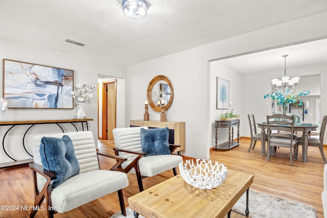 living area with light hardwood / wood-style flooring, a textured ceiling, and a notable chandelier