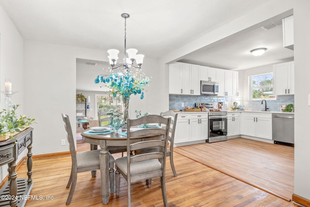 dining room with sink, light wood-type flooring, and an inviting chandelier