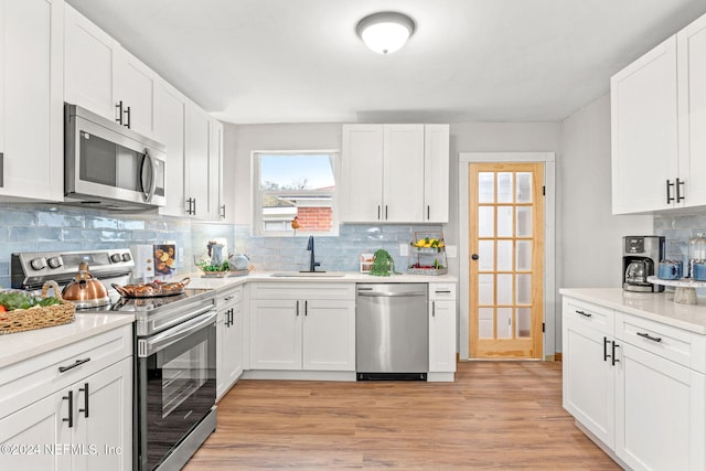 kitchen with sink, appliances with stainless steel finishes, tasteful backsplash, light hardwood / wood-style floors, and white cabinetry