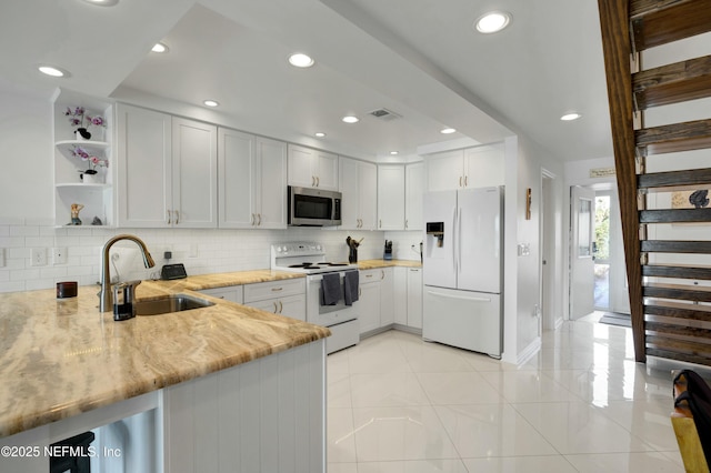 kitchen with white cabinetry, sink, kitchen peninsula, light stone countertops, and white appliances