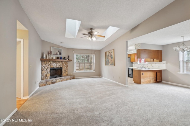 living room with ceiling fan with notable chandelier, vaulted ceiling with skylight, light carpet, and a stone fireplace