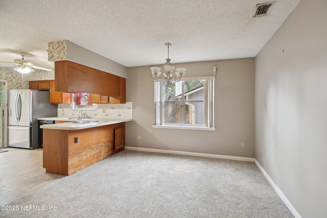 kitchen with stainless steel refrigerator, kitchen peninsula, ceiling fan with notable chandelier, decorative light fixtures, and tasteful backsplash