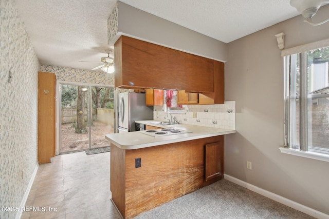 kitchen with sink, ceiling fan, kitchen peninsula, stainless steel refrigerator, and backsplash