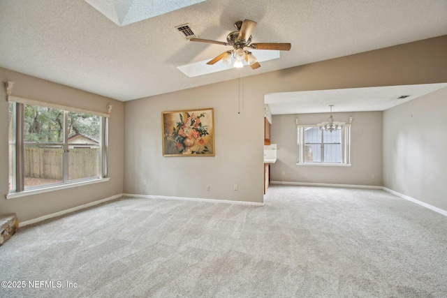 unfurnished living room with ceiling fan with notable chandelier, a textured ceiling, lofted ceiling with skylight, and light carpet