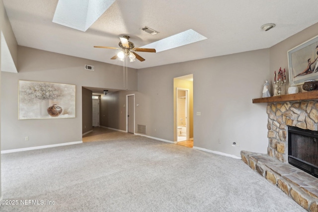 carpeted living room with a stone fireplace, ceiling fan, and a skylight