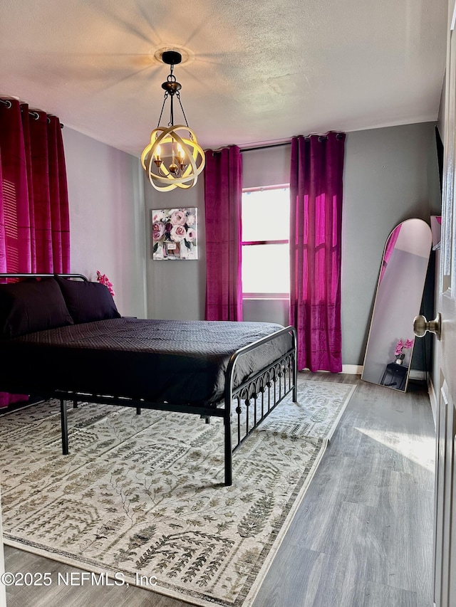 bedroom with hardwood / wood-style floors, a textured ceiling, and a notable chandelier