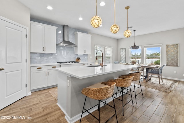 kitchen featuring a breakfast bar area, white cabinetry, hanging light fixtures, a center island with sink, and wall chimney exhaust hood