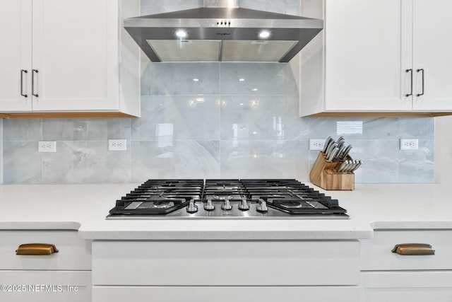 kitchen with wall chimney range hood, decorative backsplash, stainless steel gas cooktop, and white cabinets