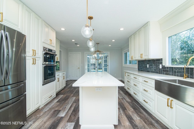 kitchen with white cabinets, ornamental molding, hanging light fixtures, a kitchen island, and appliances with stainless steel finishes