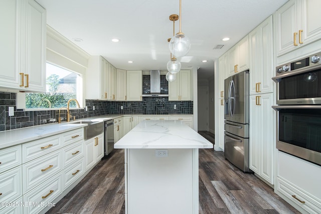 kitchen with sink, light stone counters, wall chimney exhaust hood, a kitchen island, and appliances with stainless steel finishes