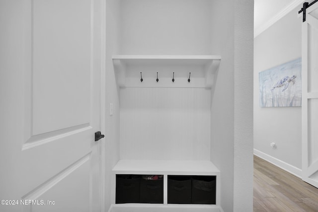 mudroom with a barn door, crown molding, and light hardwood / wood-style flooring