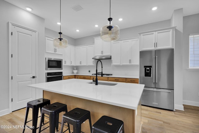 kitchen with white cabinets, decorative light fixtures, a kitchen island with sink, and appliances with stainless steel finishes