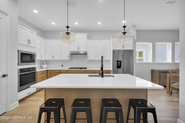 kitchen featuring sink, hanging light fixtures, an island with sink, white cabinetry, and stainless steel appliances