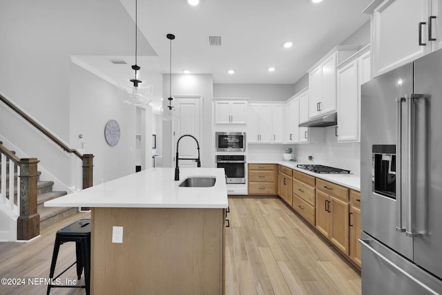 kitchen with appliances with stainless steel finishes, sink, decorative light fixtures, white cabinets, and an island with sink