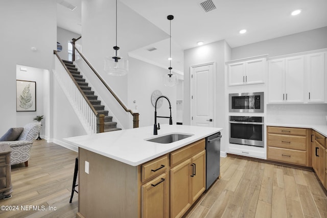 kitchen featuring stainless steel appliances, a kitchen island with sink, sink, white cabinets, and hanging light fixtures