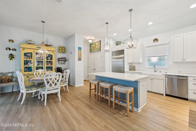 kitchen with backsplash, stainless steel appliances, white cabinets, a kitchen island, and hanging light fixtures