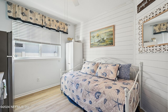 bedroom with ceiling fan, wood walls, and stainless steel refrigerator