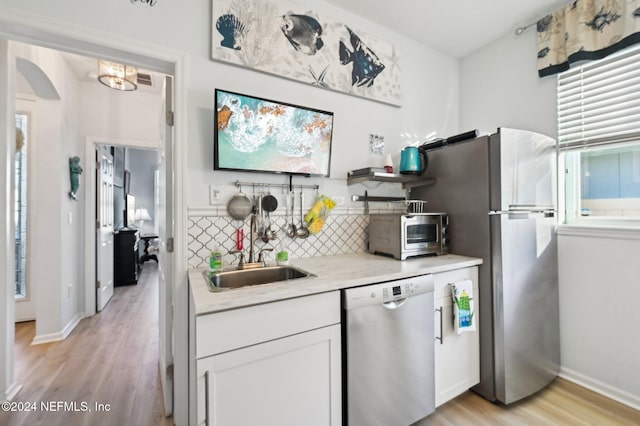 kitchen with white cabinets, appliances with stainless steel finishes, backsplash, and light hardwood / wood-style floors