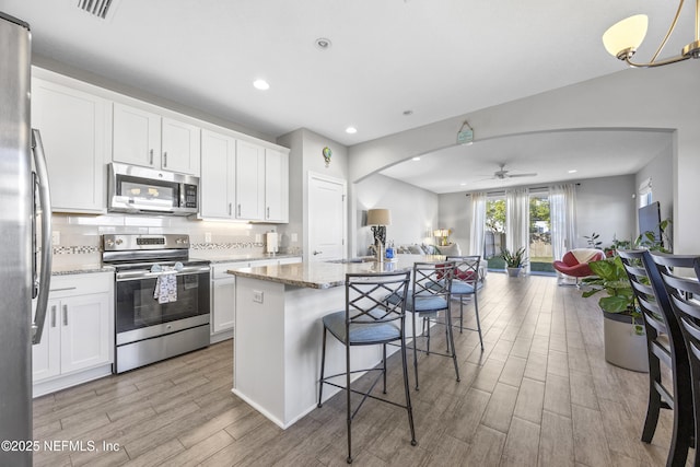 kitchen with an island with sink, white cabinets, stainless steel appliances, and light stone counters