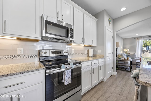 kitchen featuring white cabinets, appliances with stainless steel finishes, light hardwood / wood-style flooring, and light stone counters