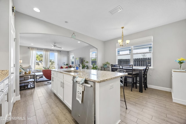 kitchen with sink, hanging light fixtures, light stone counters, a kitchen island with sink, and white cabinets