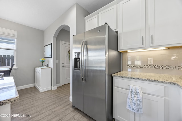 kitchen featuring backsplash, light stone countertops, white cabinetry, and stainless steel refrigerator with ice dispenser