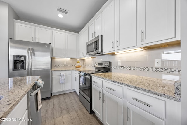 kitchen featuring light stone countertops, light hardwood / wood-style floors, decorative backsplash, white cabinets, and appliances with stainless steel finishes