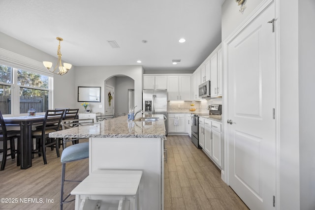 kitchen with light wood-type flooring, stainless steel appliances, pendant lighting, a center island with sink, and white cabinetry