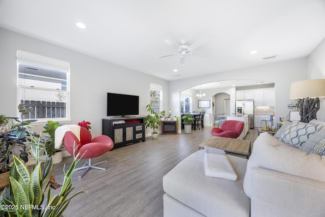 living room featuring ceiling fan with notable chandelier and light wood-type flooring