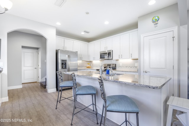 kitchen with light wood-type flooring, tasteful backsplash, light stone counters, stainless steel appliances, and white cabinetry