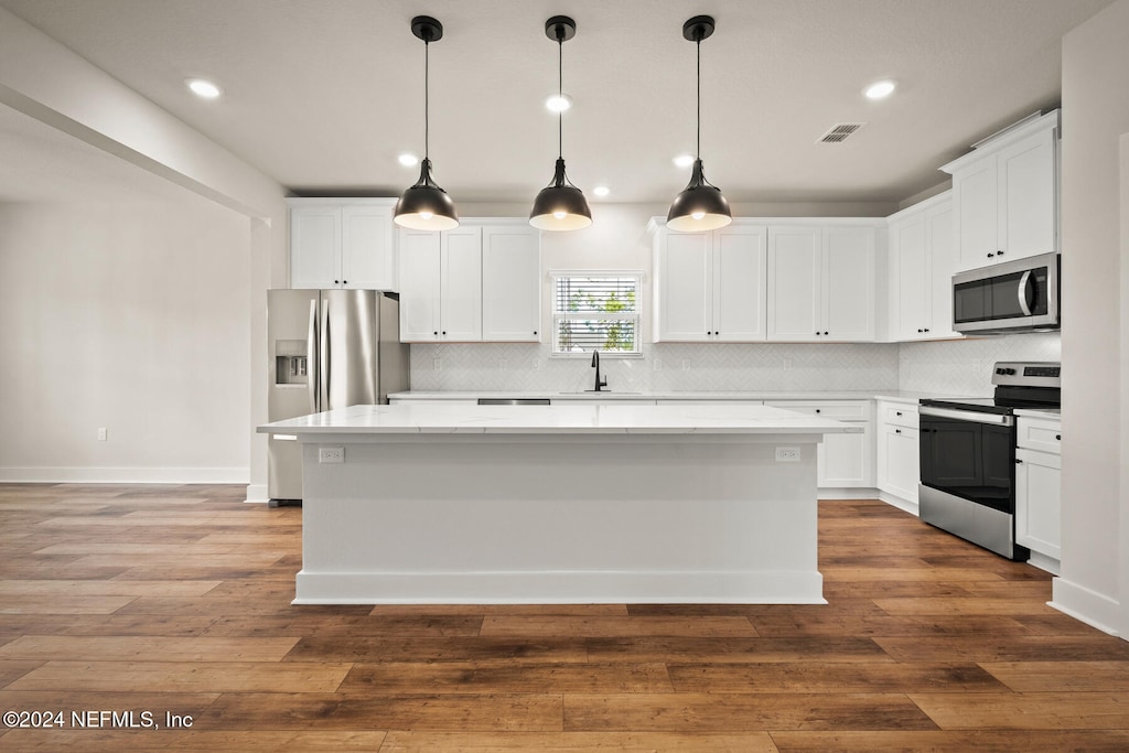 kitchen with white cabinets, appliances with stainless steel finishes, decorative light fixtures, and a kitchen island