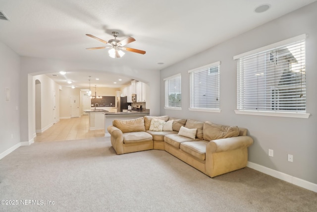 living room featuring light carpet, ceiling fan with notable chandelier, and sink