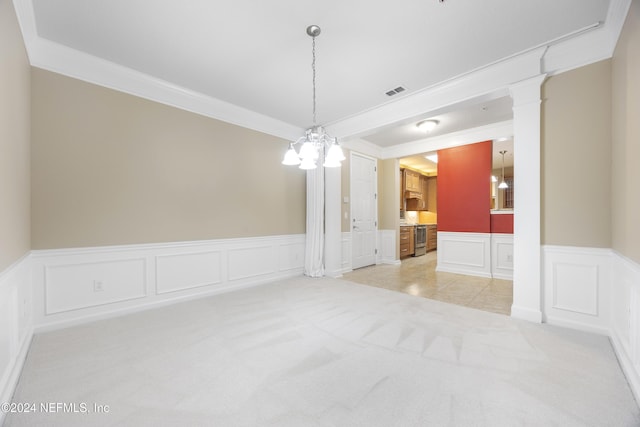 carpeted empty room with decorative columns, crown molding, and a notable chandelier