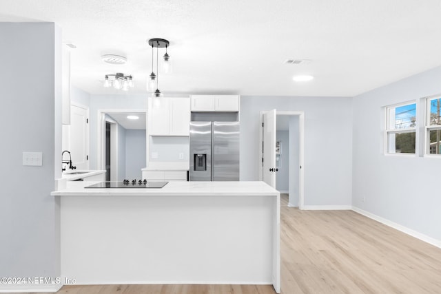 kitchen with kitchen peninsula, stainless steel fridge, pendant lighting, black electric cooktop, and white cabinets