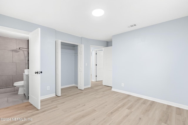 unfurnished bedroom featuring light hardwood / wood-style flooring, ensuite bath, and a closet