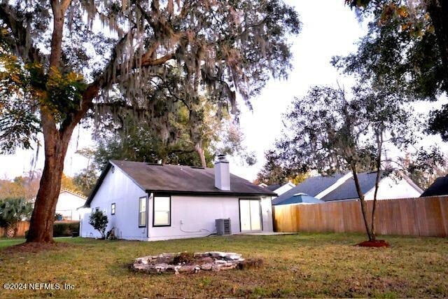 rear view of property featuring a yard, central AC unit, and a fire pit