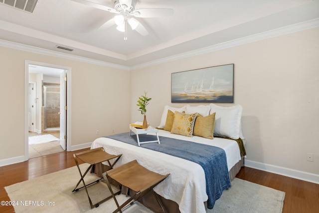 bedroom with ceiling fan, wood-type flooring, a raised ceiling, and ensuite bath