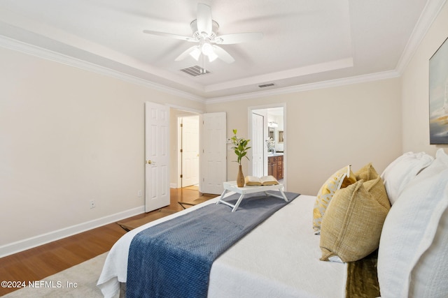 bedroom with ensuite bathroom, hardwood / wood-style floors, ceiling fan, a tray ceiling, and ornamental molding