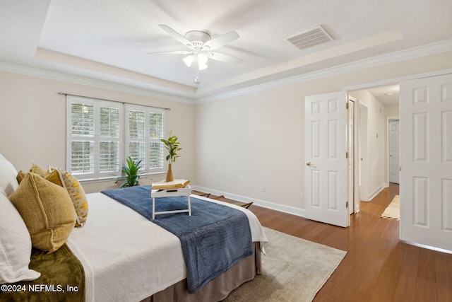 bedroom featuring a raised ceiling, ceiling fan, dark wood-type flooring, and crown molding