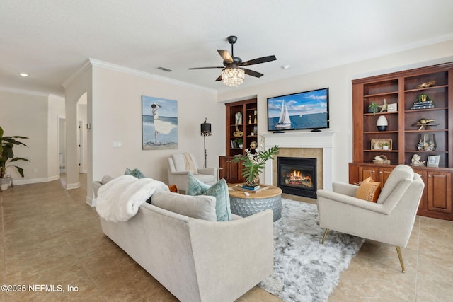 living area with built in shelves, visible vents, arched walkways, a tiled fireplace, and crown molding