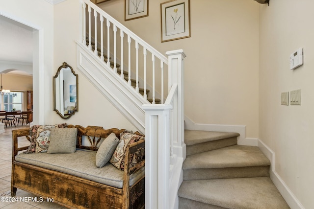 stairway with crown molding, tile patterned flooring, and a notable chandelier