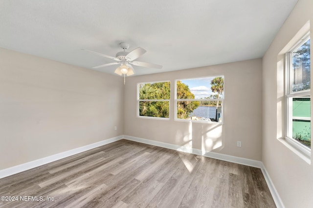 unfurnished room with ceiling fan, a water view, and light hardwood / wood-style flooring