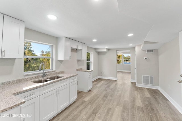 kitchen with white cabinets, sink, ceiling fan, light stone countertops, and light hardwood / wood-style floors